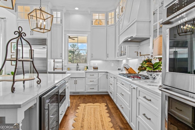 kitchen with dark wood-type flooring, custom range hood, stainless steel appliances, white cabinets, and decorative light fixtures