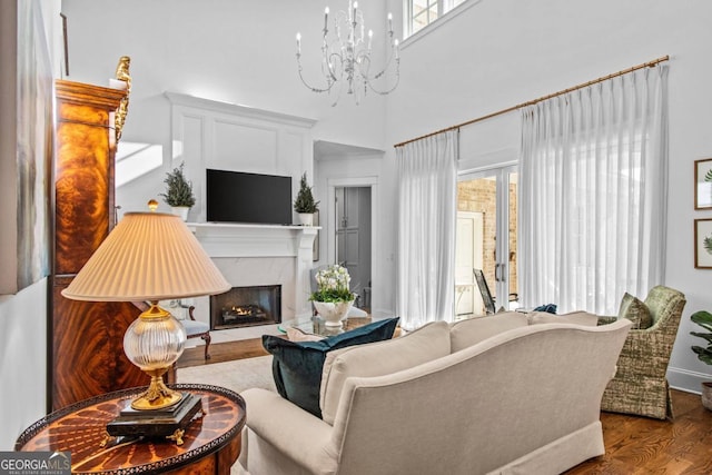 living room with a notable chandelier, wood-type flooring, and a high end fireplace