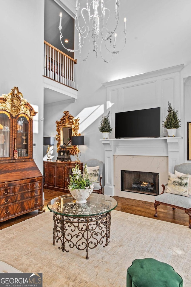 living room featuring wood-type flooring, a towering ceiling, an inviting chandelier, and a fireplace