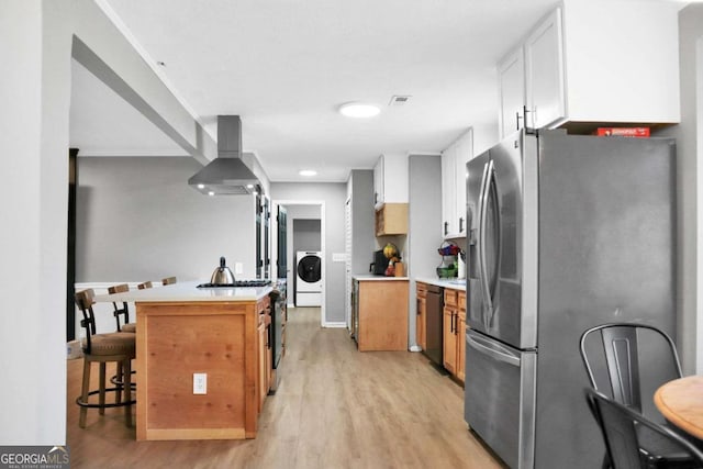 kitchen with white cabinets, stainless steel appliances, washer / clothes dryer, light hardwood / wood-style flooring, and wall chimney exhaust hood