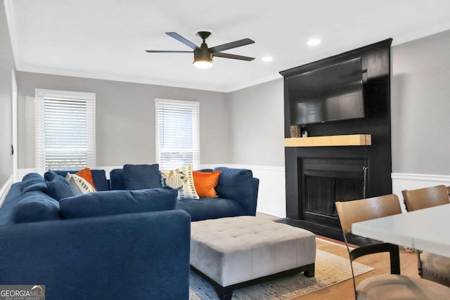 living room featuring crown molding, a large fireplace, wood-type flooring, and ceiling fan