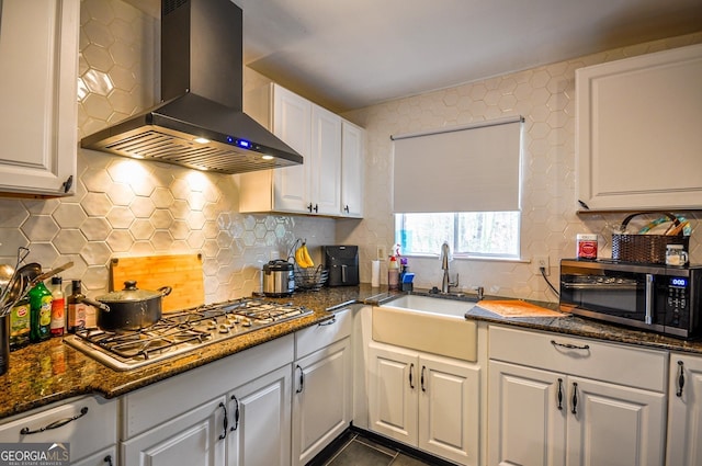 kitchen with wall chimney exhaust hood, appliances with stainless steel finishes, white cabinetry, and backsplash