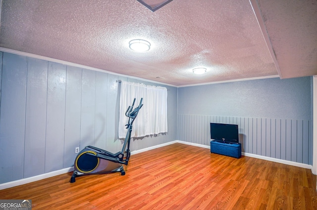 workout area with light hardwood / wood-style flooring, crown molding, and a textured ceiling