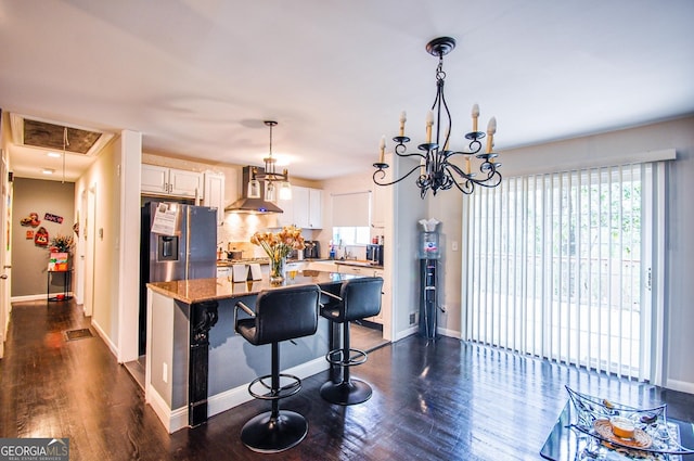 kitchen featuring wall chimney exhaust hood, decorative light fixtures, light stone countertops, dark hardwood / wood-style flooring, and white cabinetry