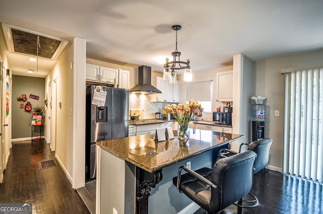 kitchen featuring appliances with stainless steel finishes, hanging light fixtures, wall chimney exhaust hood, white cabinetry, and dark hardwood / wood-style flooring