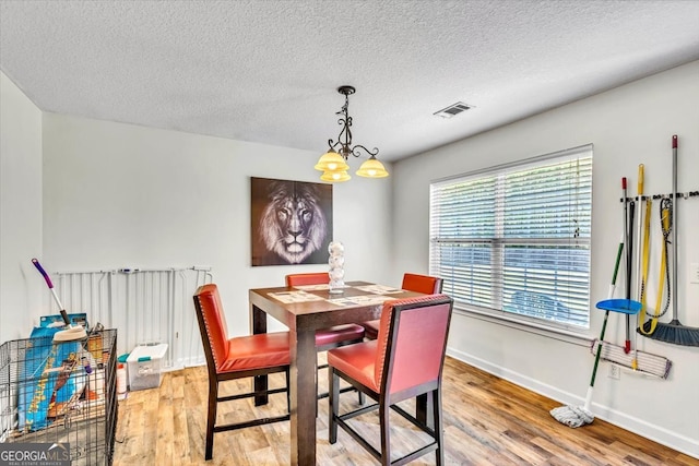 dining space featuring light hardwood / wood-style floors, a textured ceiling, and a notable chandelier