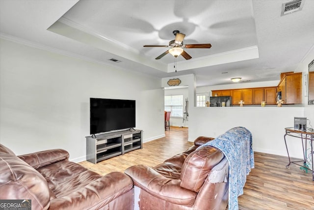 living room with ceiling fan, a tray ceiling, and light hardwood / wood-style floors