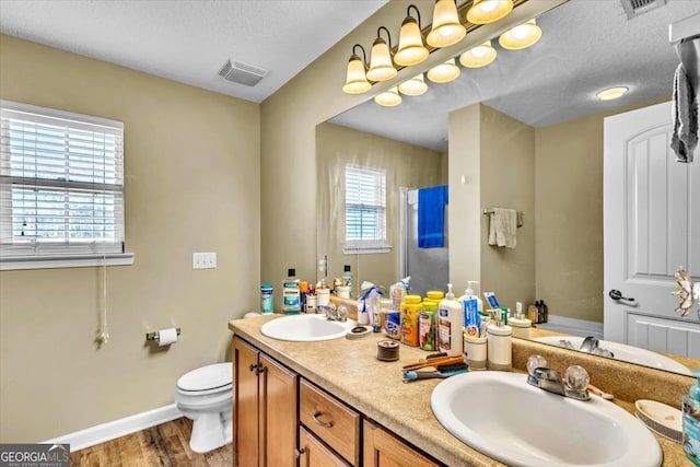 bathroom with toilet, vanity with extensive cabinet space, dual sinks, a textured ceiling, and hardwood / wood-style flooring