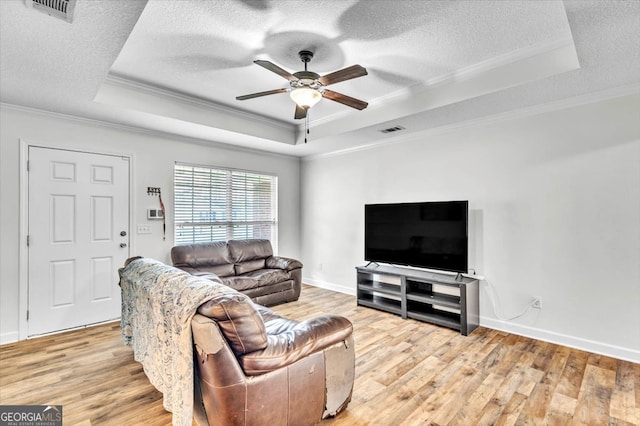 living room featuring ceiling fan, a raised ceiling, light hardwood / wood-style floors, a textured ceiling, and ornamental molding