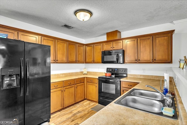 kitchen featuring sink, light wood-type flooring, black appliances, and a textured ceiling