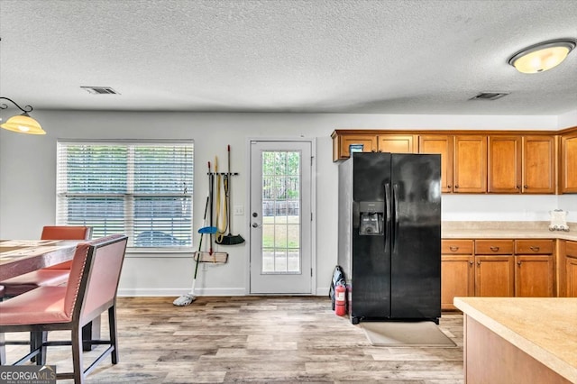 kitchen with a textured ceiling, pendant lighting, black fridge, and light hardwood / wood-style flooring