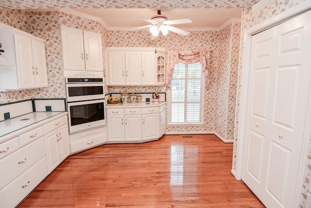 kitchen featuring light hardwood / wood-style floors, white cabinets, crown molding, ceiling fan, and multiple ovens