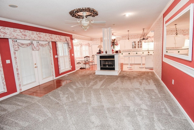 unfurnished living room with french doors, crown molding, ceiling fan, and light colored carpet