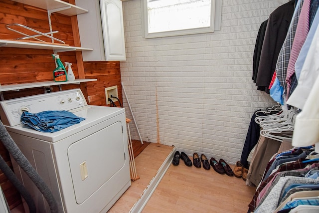 laundry area featuring light wood-type flooring, brick wall, and washer / clothes dryer