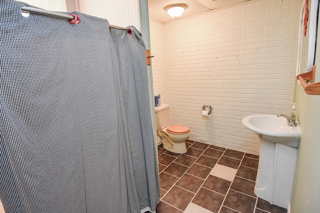 bathroom featuring tile flooring, brick wall, and toilet