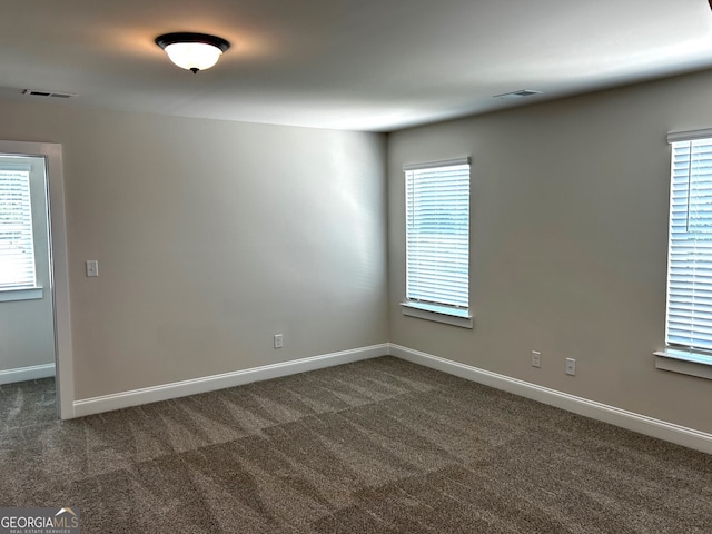 unfurnished room with baseboards, visible vents, and dark carpet