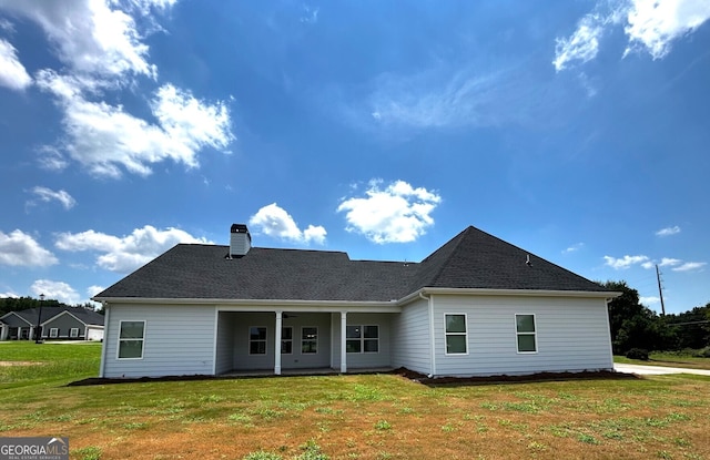 back of house featuring a shingled roof, a chimney, a ceiling fan, and a yard