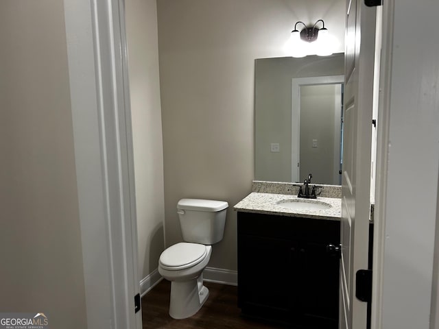 half bath featuring baseboards, vanity, toilet, and wood finished floors