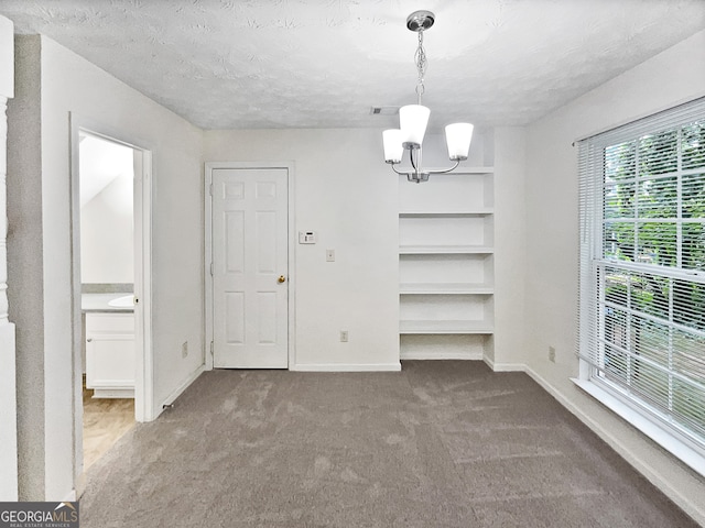 unfurnished dining area featuring a textured ceiling, carpet, and a chandelier