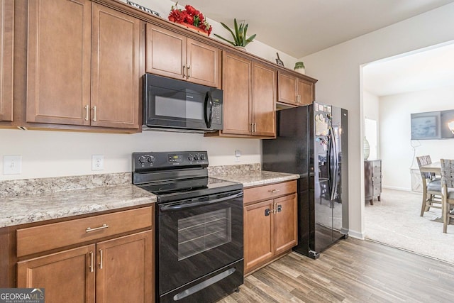 kitchen featuring light stone countertops, black appliances, and light wood-type flooring