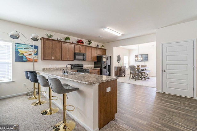 kitchen featuring a kitchen breakfast bar, pendant lighting, dark carpet, and black appliances