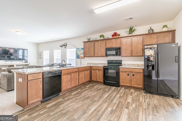 kitchen featuring kitchen peninsula, light stone countertops, hardwood / wood-style floors, black appliances, and sink