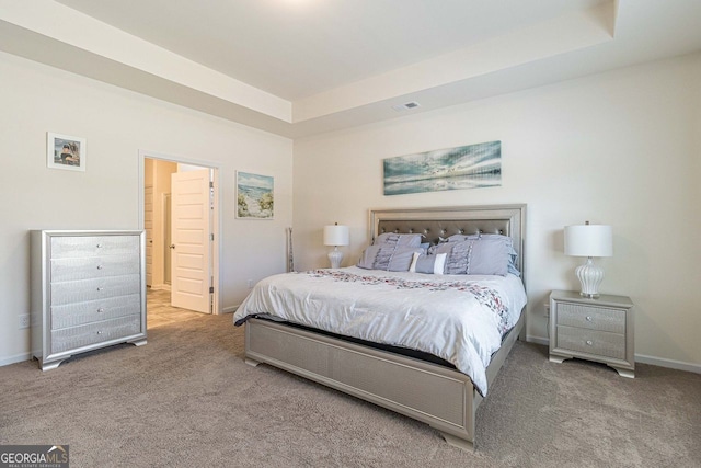 carpeted bedroom with ensuite bathroom and a raised ceiling