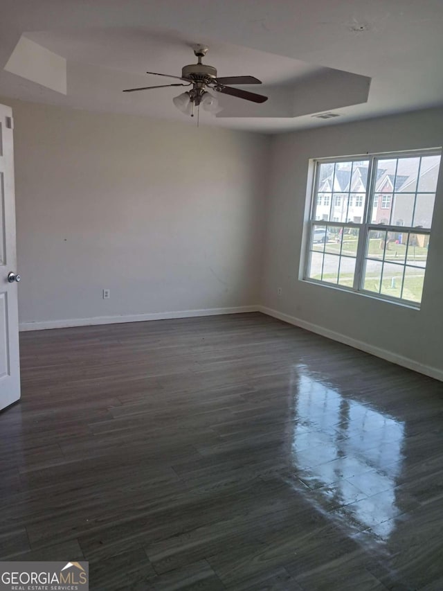 unfurnished room with ceiling fan, a raised ceiling, and dark wood-type flooring