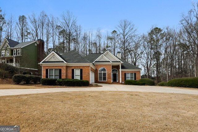 view of front of house featuring driveway, brick siding, a chimney, and a front lawn