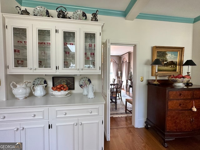 bar with white cabinets, dark wood-type flooring, ornamental molding, and beam ceiling