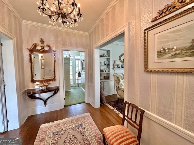 hall featuring built in shelves, crown molding, dark wood-type flooring, and an inviting chandelier