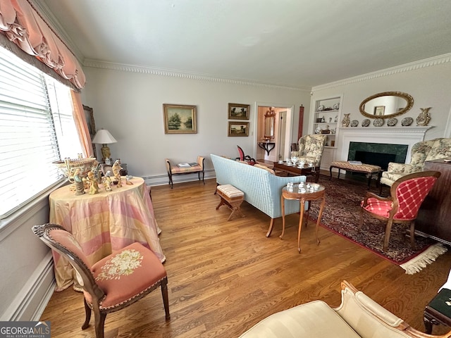 living room featuring built in shelves, a baseboard radiator, light wood-type flooring, and crown molding