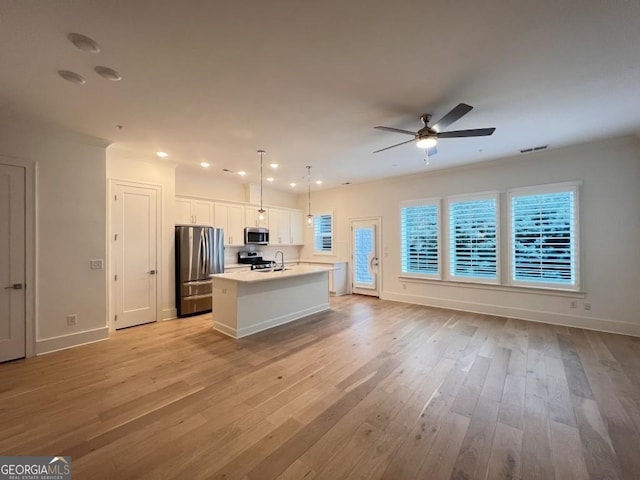 kitchen with appliances with stainless steel finishes, pendant lighting, ceiling fan, light hardwood / wood-style floors, and a center island with sink