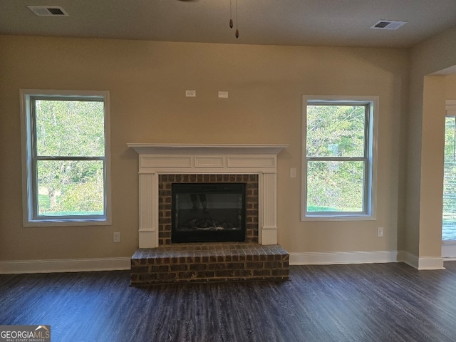 unfurnished living room with a brick fireplace, a wealth of natural light, and dark hardwood / wood-style flooring