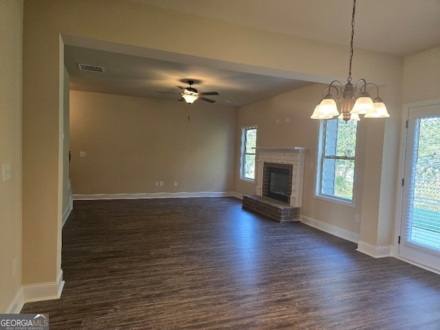 unfurnished living room with a healthy amount of sunlight, a fireplace, ceiling fan with notable chandelier, and dark hardwood / wood-style flooring