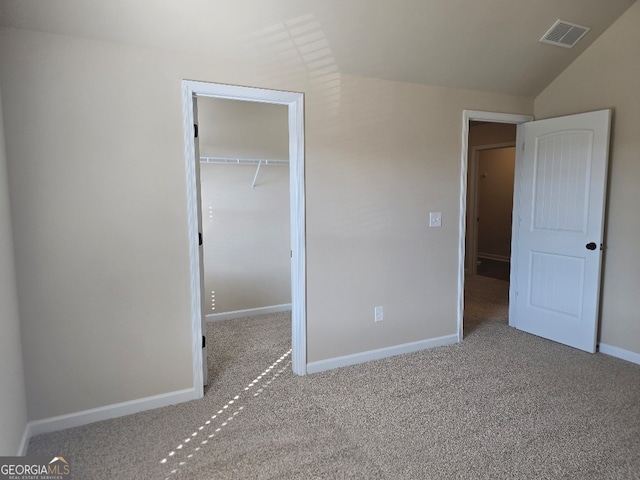 unfurnished bedroom featuring lofted ceiling, a closet, a walk in closet, and light colored carpet