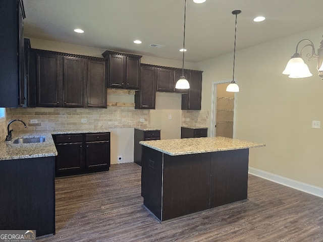 kitchen with light stone counters, dark wood-type flooring, sink, a kitchen island, and decorative light fixtures