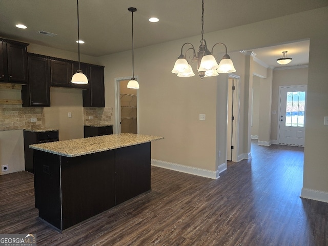 kitchen with light stone counters, hanging light fixtures, a kitchen island, dark brown cabinets, and dark hardwood / wood-style flooring