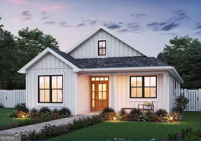 view of front facade featuring board and batten siding, a shingled roof, a front lawn, and fence