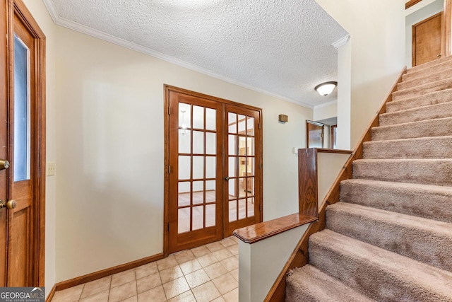 entrance foyer featuring a textured ceiling, ornamental molding, light tile floors, and french doors