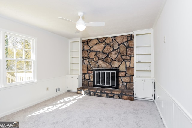 unfurnished living room featuring built in shelves, visible vents, ornamental molding, light carpet, and a stone fireplace