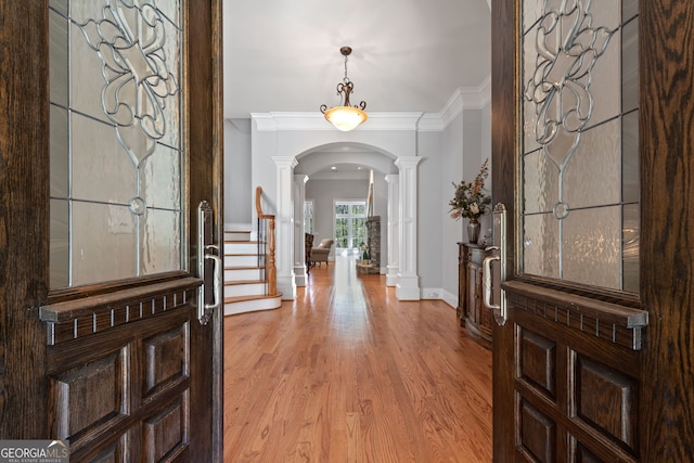 foyer entrance featuring light hardwood / wood-style floors, decorative columns, and crown molding