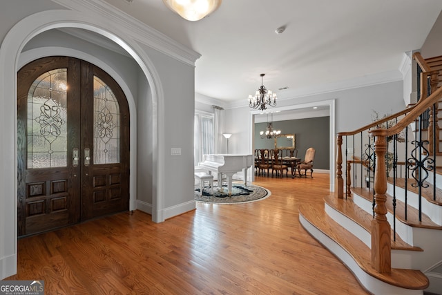 foyer entrance featuring a notable chandelier, ornamental molding, and wood-type flooring