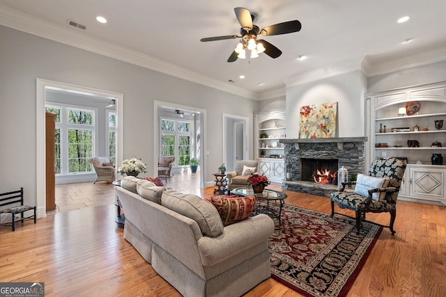 living room featuring light hardwood / wood-style flooring, a fireplace, built in features, ceiling fan, and ornamental molding