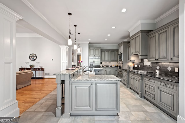 kitchen featuring gray cabinetry, a center island with sink, light stone countertops, appliances with stainless steel finishes, and sink