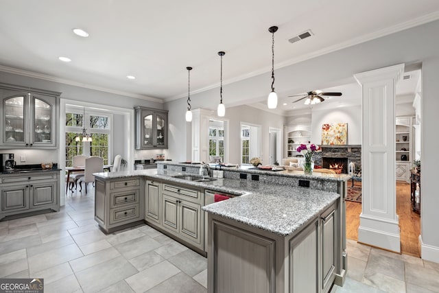 kitchen with decorative light fixtures, light hardwood / wood-style flooring, a fireplace, ceiling fan, and an island with sink