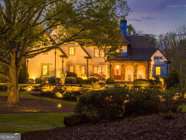 back house at dusk featuring a lawn