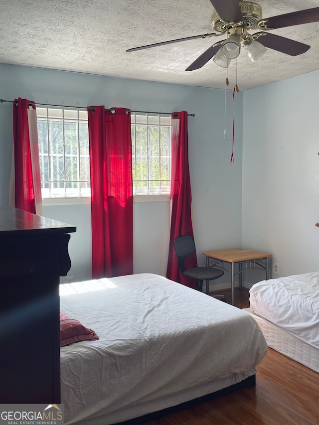 bedroom featuring dark wood-type flooring, ceiling fan, and a textured ceiling