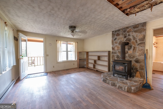 unfurnished living room with a textured ceiling, wood-type flooring, a baseboard heating unit, and a wood stove