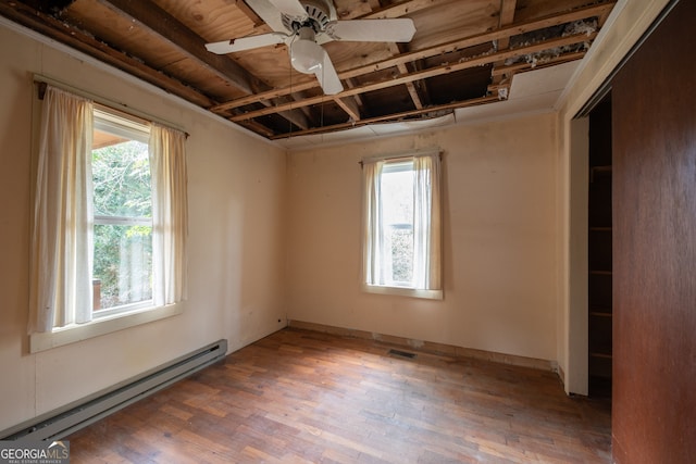 empty room featuring a healthy amount of sunlight, hardwood / wood-style floors, ceiling fan, and baseboard heating